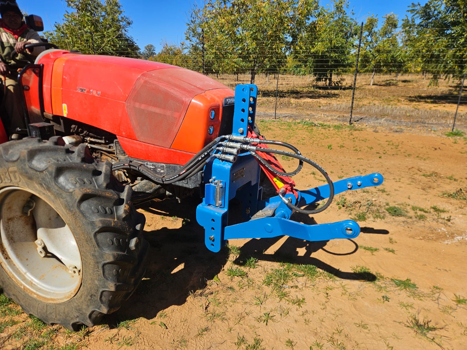 Red tractor with a blue hydraulic mounting attachment at the head of an orchard row