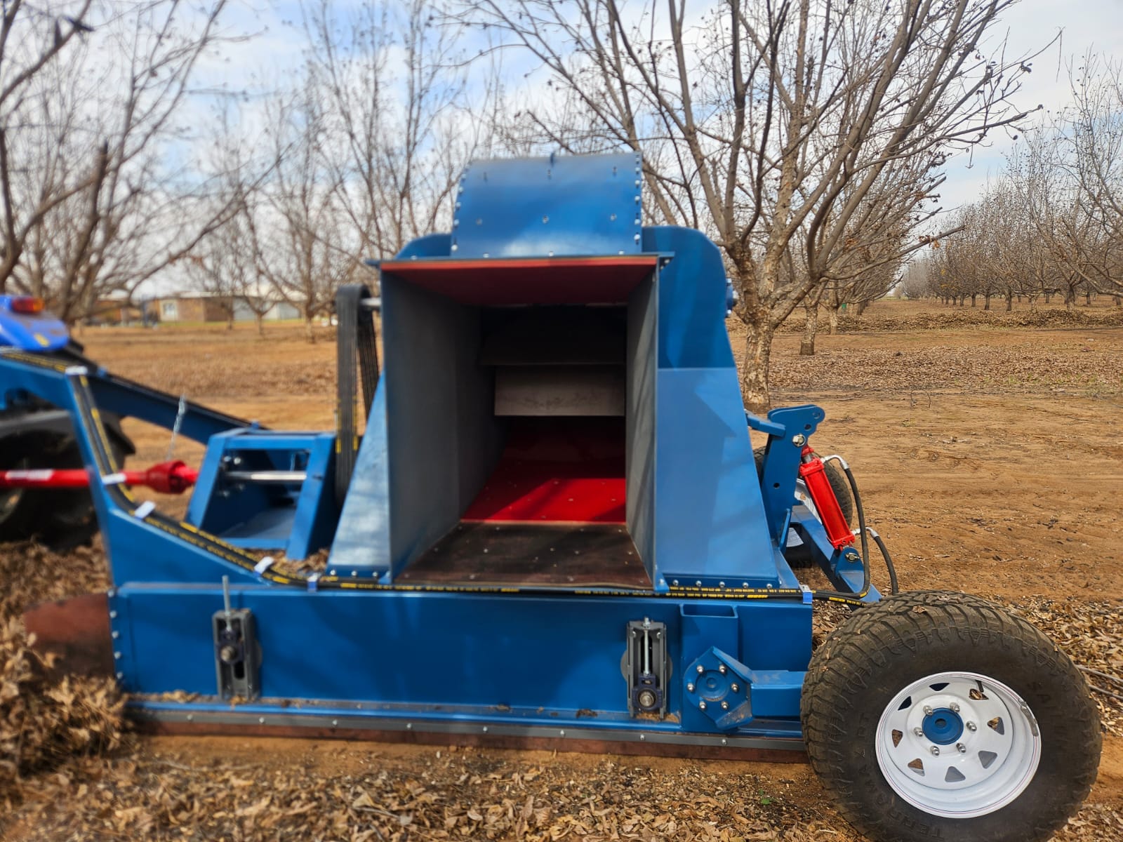 Blue SMJ tree shaker implement in a pecan orchard between tree rows