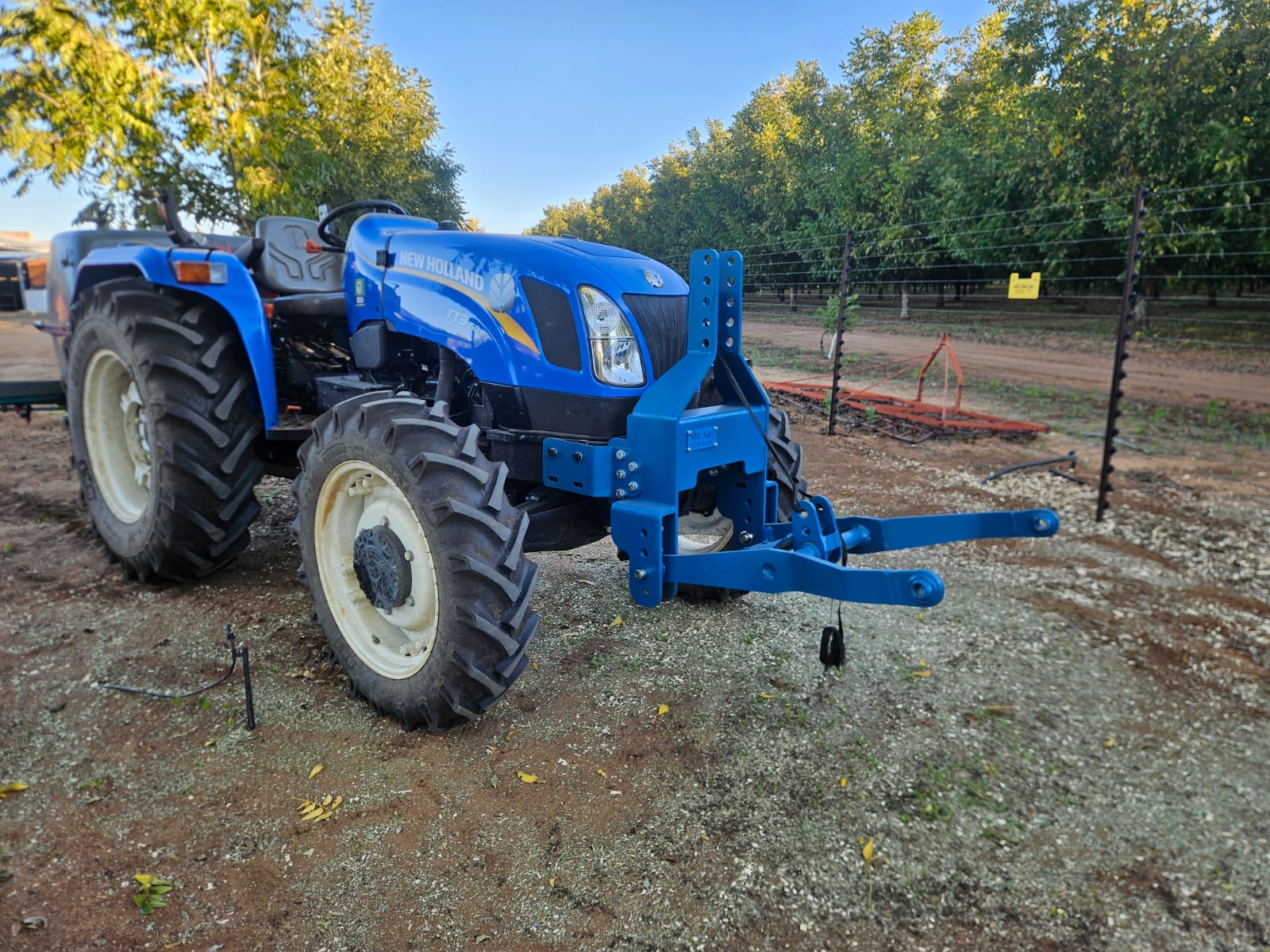 SMJ tree shaker mounted on the front of a tractor between orchard rows