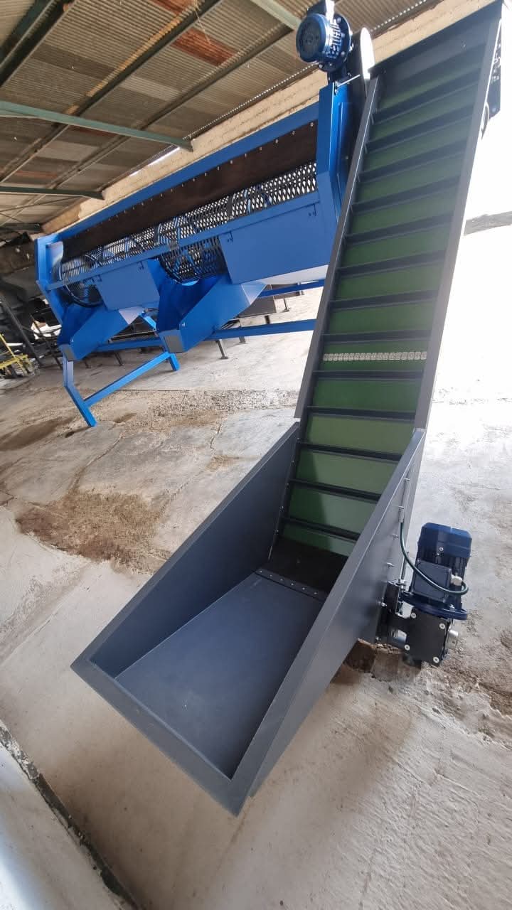 Blue nut cleaning drum and green elevator conveyor in a workshop