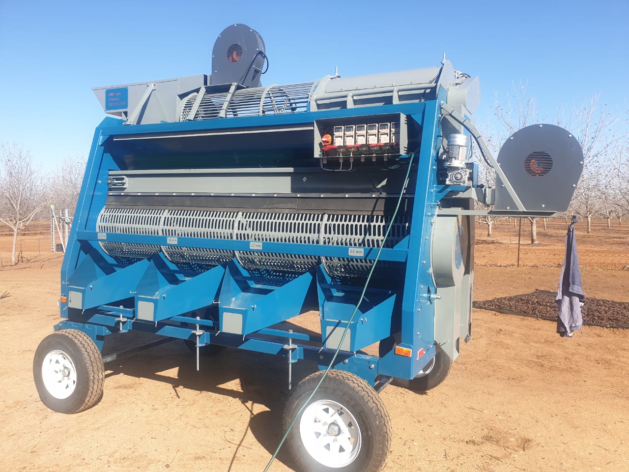 Wheeled nut-sorting machine with perforated rotary drums and chutes in an orchard