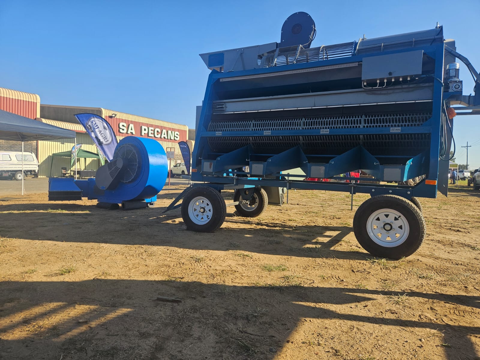 Wheeled nut-sorting machine and a large blue blower fan on a dirt lot in front of a SA Pecans building
