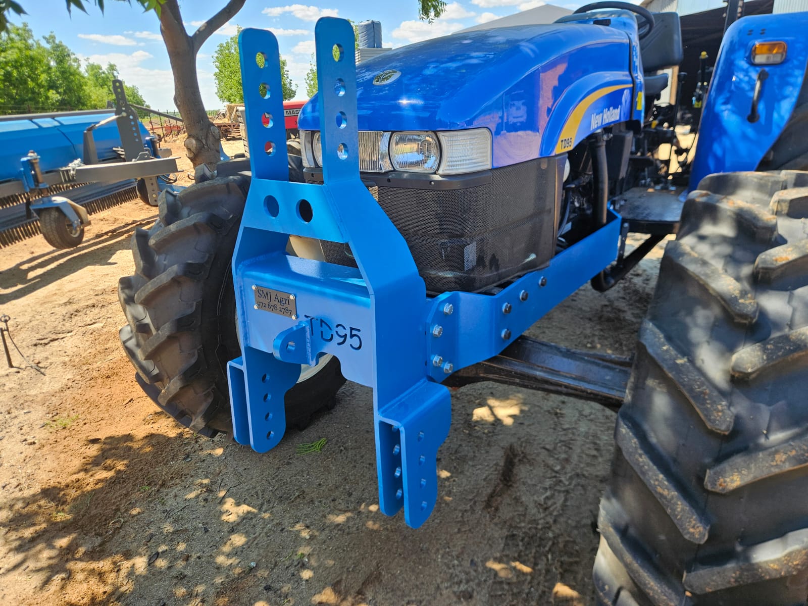 Blue tractor with a custom blue front hitch bracket standing in a farm yard