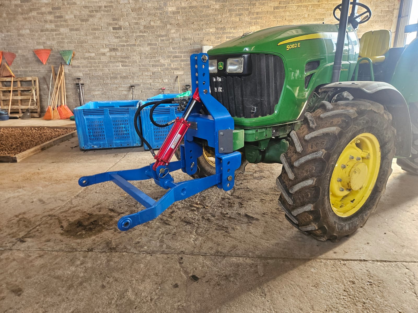 Tractor with a blue and red front hydraulic hitch parked inside a brick barn